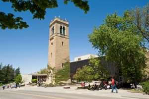 Trees and pedestrians frame a view of the Carillon Tower in front of the Sewell Social Sciences building