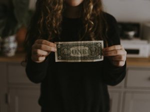 Photo of a woman holding a one dollar bill.
