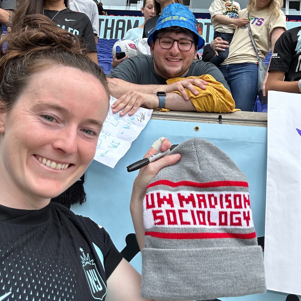 Rose Lavelle holding a UW-Madison Sociology hat with Raphy Jacobson behind her.