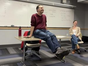 Eric Grodsky sitting on a desk in a classroom.
