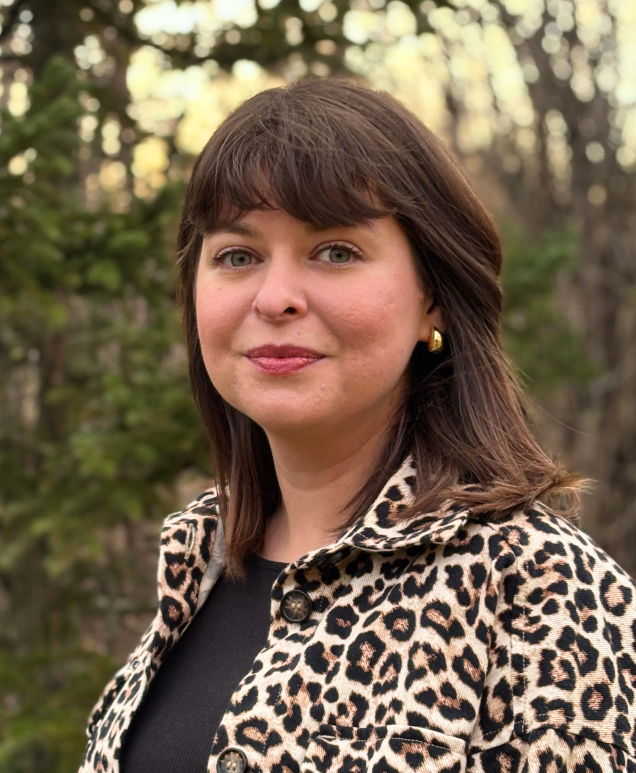 Headshot of Kristina, a woman with shoulder length brown hair wearing a leopard print jacket. 